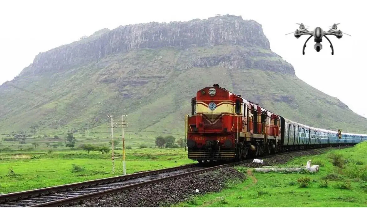 A train running through green hills with a survey drone overhead